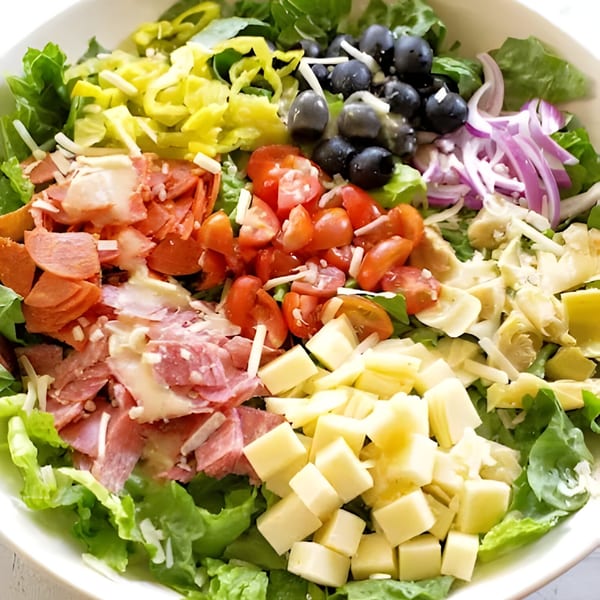 Close-up of a vibrant Italian salad with lettuce, pepperoni, tomatoes, olives, cheese, and artichoke hearts.