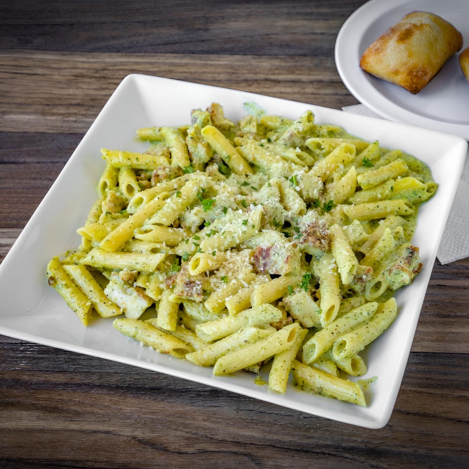 Bianco's Italian Cuisine penne pasta with pesto sauce, parmesan cheese, and chicken, served with bread.